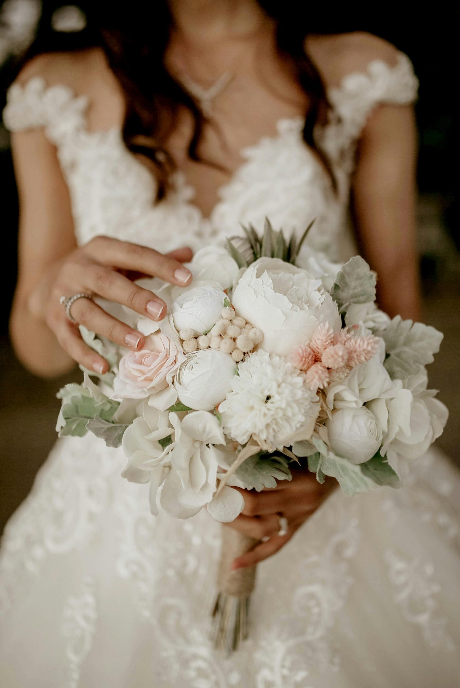 Close-up of a bride holding a delicate white and pink floral bouquet, showcasing wedding elegance.